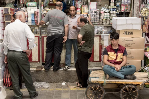 TEHRAN, IRAN - AUGUST 14, 2016: Merchants and delivery boys having a break and discussing in a covered street of Tehran bazaar — Stock Photo, Image