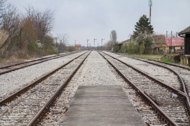 Sırbistan 'ın Palic kentindeki kırsal bir tren istasyonundaki tren rayları, rayları ve platformlar, semafor sinyallerine yönelik bir perspektifle soğuk, gri ve bulutlu bir kış öğleden sonrasında çekildi