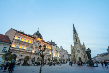 NOVI SAD, SERBIA - 26 Kasım 2016: The Name of Mary Church, Novi Sad katolik katedrali, alacakaranlıkta Trg Slobode Meydanı 'nda yürüyen bir kalabalıkla. Bu katedral Novi Sad 'ın simgesidir.