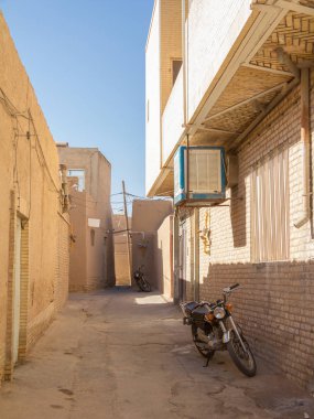 Tipik kil duvarları ve binalarıyla birlikte İran 'ın Yazd kentinin tipik bir caddesinde duran iki motosiklet. Yazd, Orta İran 'ın ana şehridir.