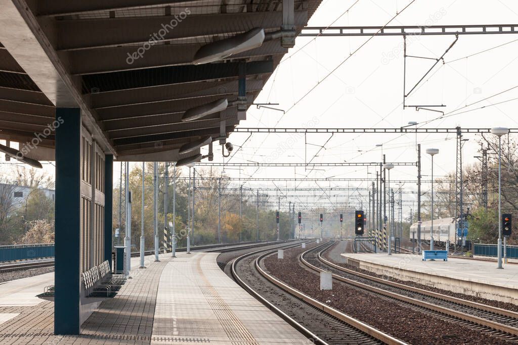 Recently reconstructed tracks on the modernized platforms of a suburban train station in a capital city of Central Europe, with brand new concrete structures signalling in the background