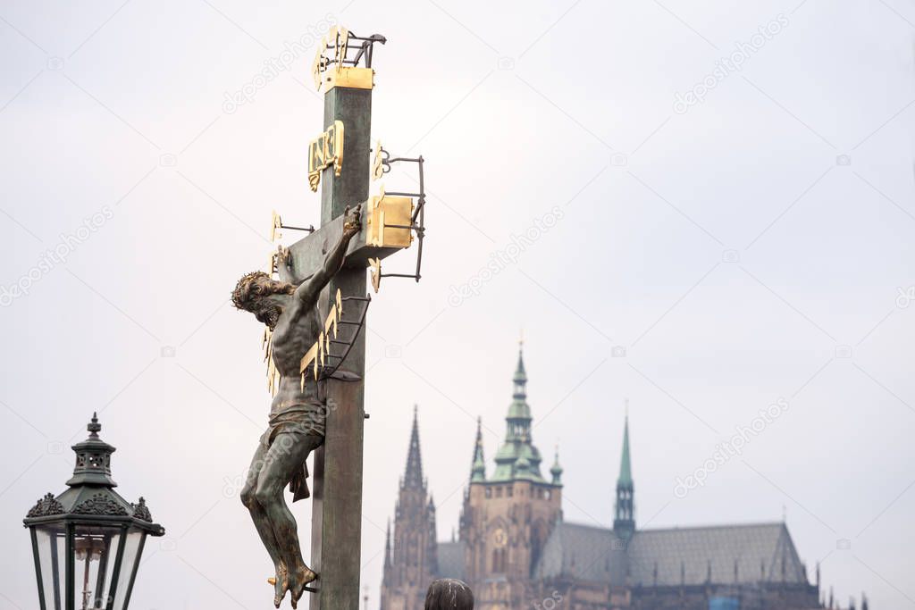 Crucifix with a statue of Jesus Christ on the cross, from the 17th century, in front of the Saint Vitus cathedran, blurred in background, a landmark of the Prague castle in czech republic