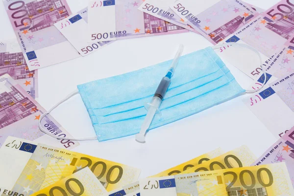 Koruyucu tıbbi maske, şırınga aşısı ve euro faturaları. Pahalı tıp konsepti.