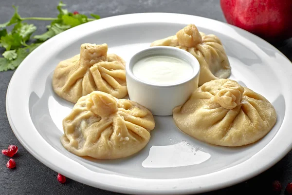 Boiled khinkali on a dark background with sauce and herbs