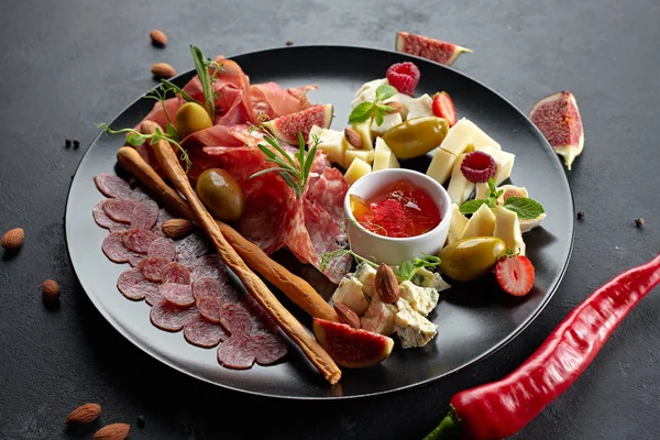 Fleisch und Käse sortiert, auf einem schwarzen Teller mit Kräutern und Beeren — Stockfoto