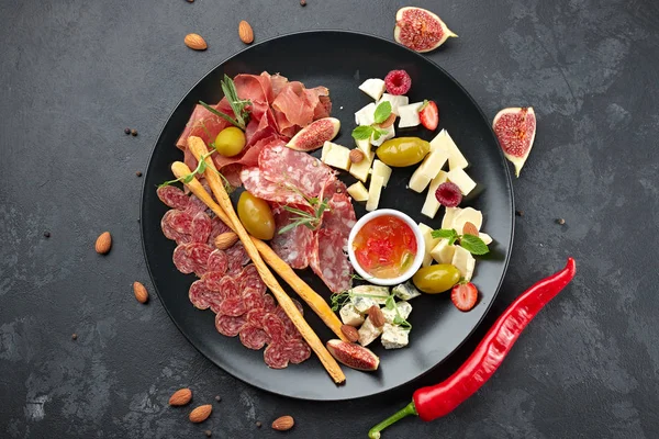 Meat and cheese assorted, on a black plate with herbs and berrie — Stock Photo, Image