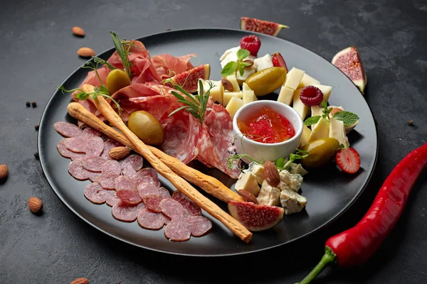 Meat and cheese assorted, on a black plate with herbs and berrie — Stock Photo, Image