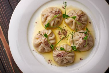 Khinkali beyaz bir tabakta, tahta bir zemin üzerinde, mikro yeşil ile. Koyu tahta arkaplan.