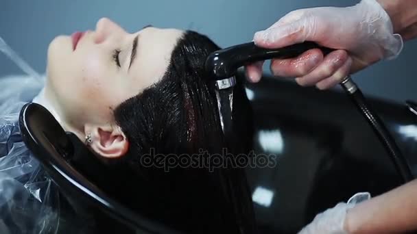 Hairdresser in gloves washing brunette girl hair over sink in beauty shop. — Stock Video