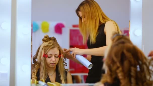 Salón de belleza. Tres modelos en salón de belleza. Las niñas se preparan para la exhibición de moda. El maquillador hace un maquillaje a la mujer de pelo rubio . — Vídeo de stock