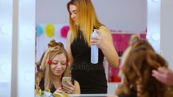 Краса, зачіска та концепція людей - щаслива молода жінка зі смартфоном та перукарнею, що робить укладання волосся в салоні — стокове відео