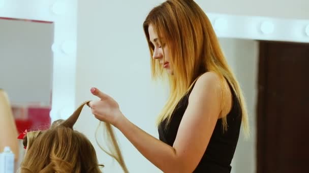 Mode-Stylist Friseur macht eine Frisur für den Kunden eines schönen jungen Mädchens in einem modischen Salon. Friseur frisiert schönes Mädchen, das in den Spiegel schaut. — Stockvideo