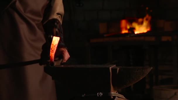 Blacksmith brings dripping hot metal from furnace and creates a shower of sparks as he beats a piece of white hot metal with a hammer on an anvil. Close up recorded. — Stockvideo