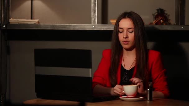 Όμορφη μελαχρινή σε ένα κόκκινο σακάκι, συνεργάζεται με το laptop του και να καπνίζει ένα ηλεκτρονικό τσιγάρο σε δημόσιο χώρο — Αρχείο Βίντεο