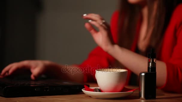 Close-up brunette in a red jacket, works with his laptop and smokes an electronic cigarette in a public place — Stock Video