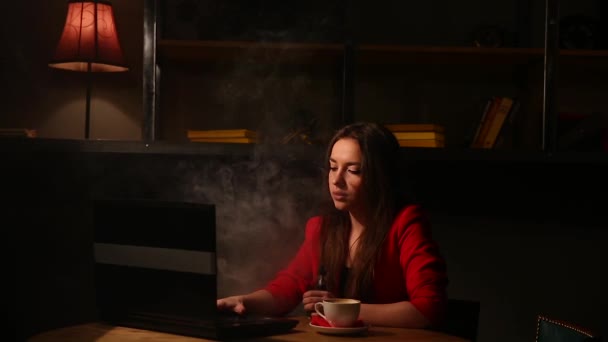Mädchen, das mit einem Laptop arbeitet und Kaffee trinkt und eine elektronische Zigarette raucht. Arbeiten aus der Ferne in einem Café. — Stockvideo