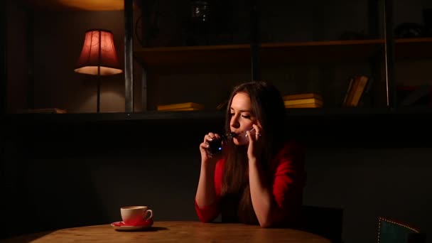 Flickan i den röda jackan röka elektronisk cigarett och talar i en mobiltelefon. — Stockvideo