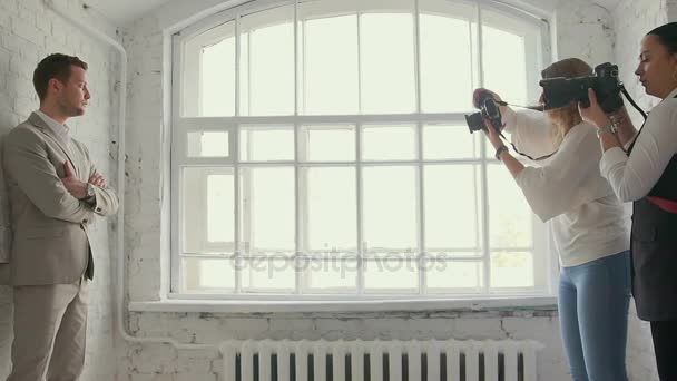 Un fotógrafo haciendo un retrato de hombre de negocios sobre un fondo de pared blanco ladrillo. Clase magistral para fotógrafos. Sesión de fotos Becxtage. Las fotografías están entrenadas . — Vídeos de Stock