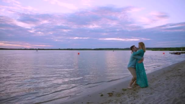 En la orilla del lago, una pareja enamorada abraza y besa. El hombre levanta y gira el talón en sus manos . — Vídeos de Stock