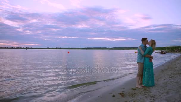 En la orilla del lago, una pareja enamorada abraza y besa. El hombre levanta y gira el talón en sus manos . — Vídeo de stock