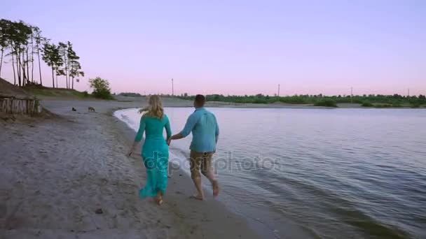 Romantiska par promenader längs en strand i solnedgången — Stockvideo