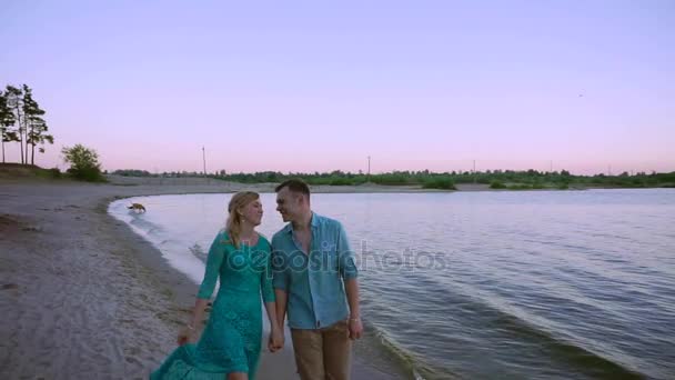 ロマンチックなカップルは夕暮れ時のビーチに沿って歩く — ストック動画