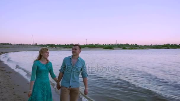 Romantic couple walking along a beach at sunset — Stock Video