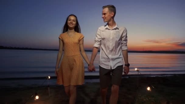 Casal caminha ao longo do cais ao pôr do sol sobre o mar — Vídeo de Stock