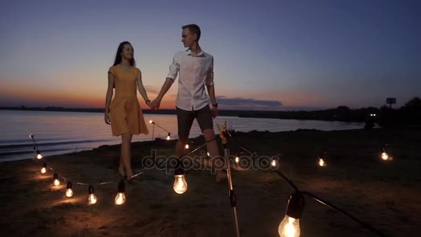 Casal caminha ao longo do cais ao pôr do sol sobre o mar — Vídeo de Stock