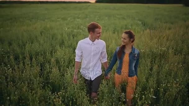 Fantastica coppia felice divertirsi in un campo sfondo tramonto. Bello ragazzo caucasico che indossa camicia a quadri abbraccia gentilmente una ragazza sorridente con i capelli biondi in camicia a quadri. Stile di vita e concetto di viaggio . — Video Stock