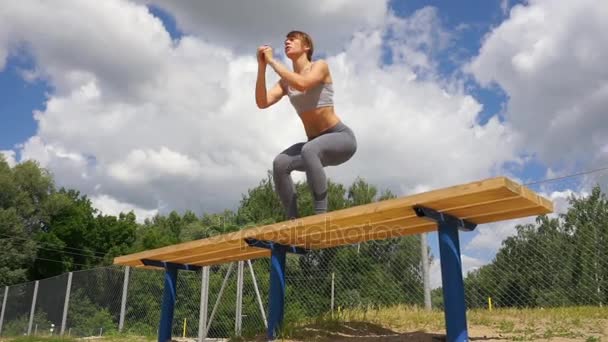 Ung passar aktiva kvinnan bänk hoppa squat hoppa på gata. Fitness tjej gör övningar utomhus — Stockvideo