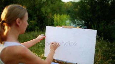 doğada tuval üzerine güzel sarışın kadın sanatçı onun elinde bir fırçayla çizer