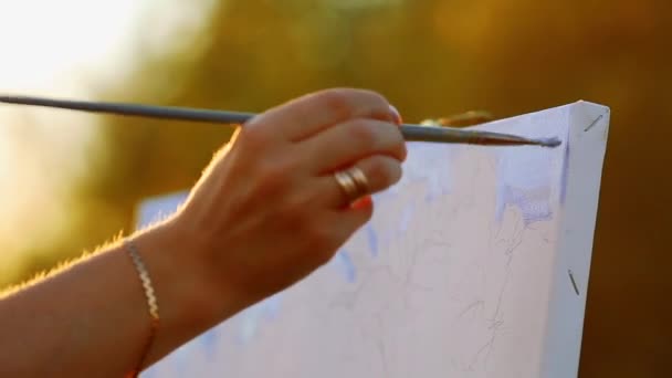 Mains de l'artiste avec un pinceau, peindre un tableau sur un chevalet en plein air — Video