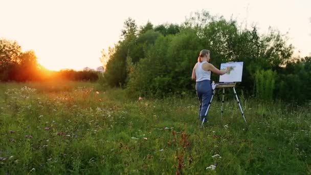 Artysta kobieta pędzlem i polytray w jej rękach rysuje na płótnie na tle przyrody. Artysta maluje na sztalugach. Artysta w pracy — Wideo stockowe