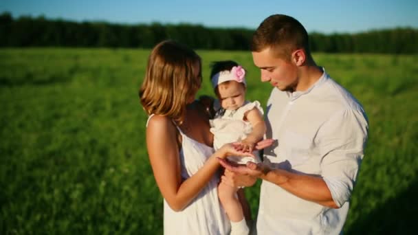 Lycklig familj. Pappa mamma och en liten flicka, promenader i ett fält klädda i vitt under den nedgående solen strålar — Stockvideo