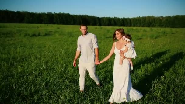 Una famiglia felice. Papà mamma e una bambina, camminando in un campo vestito di bianco sotto i raggi del sole al tramonto — Video Stock