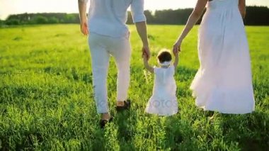 Aile parkta yürüyor ve bebek kızı onun ilk adımlarını atıyor. Beyaz ve batan güneşin altında dışarı.