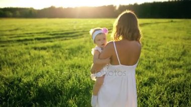 Anne ile kızı parkın içinden beyaz elbise ve kameraya bakarak gün batımında yürür.