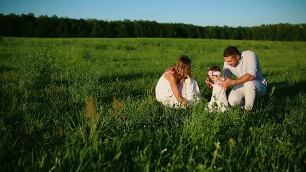 Una famiglia felice. Papà mamma e una bambina, camminando in un campo vestito di bianco sotto i raggi del sole al tramonto — Video Stock