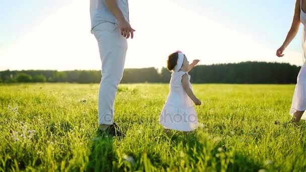 Familienspaziergänge im Park und die kleine Tochter macht ihre ersten Schritte. ganz in weiß und unter der untergehenden Sonne. — Stockvideo