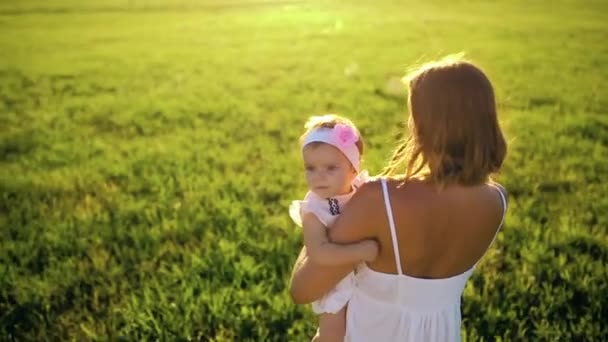 Mère marche avec sa fille à travers le parc au coucher du soleil dans une robe blanche et en regardant la caméra . — Video