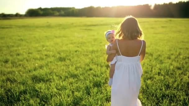 Μητέρα βόλτες με την κόρη της μέσα από το πάρκο στο ηλιοβασίλεμα σε ένα λευκό φόρεμα και εξετάζοντας τη φωτογραφική μηχανή. — Αρχείο Βίντεο