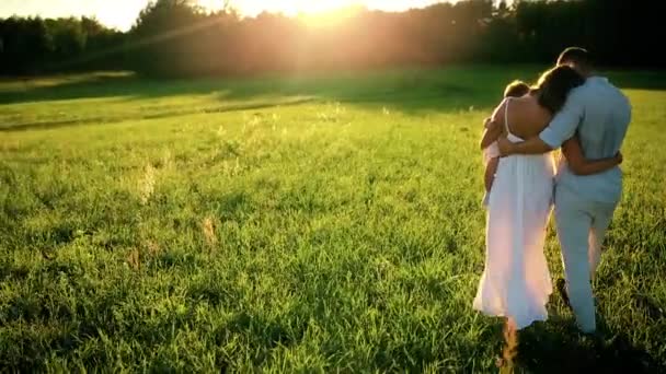 Una famiglia felice. Papà mamma e una bambina, camminando in un campo vestito di bianco sotto i raggi del sole al tramonto — Video Stock