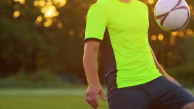 Profesyonel bir futbolcu ve yeşil Üniformalı erkeklere, diz futbol topu dengelemek.