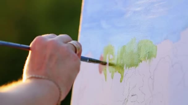 Handen van de kunstenaar met een borstel, beeld een op een ezel in de open lucht — Stockvideo
