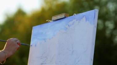 Eller sanatçının bir fırça ile boya bir resim açık havada bir şövale üzerinde