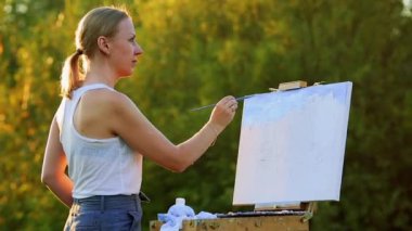 Coşku kızla boyalar bir kağıda bir manzara çizer.