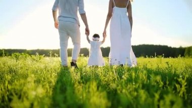 Aile parkta yürüyor ve bebek kızı onun ilk adımlarını atıyor. Beyaz ve batan güneşin altında dışarı.