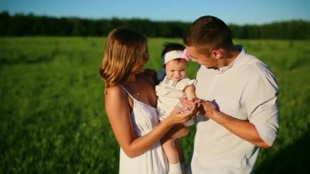 Счастливая семья. Папа мама и маленькая девочка, прогуливаясь в поле, одетые в белое под лучами заходящего солнца — стоковое видео