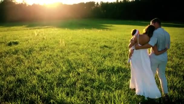 Familia feliz. Papá mamá y una niña, caminando en un campo vestido de blanco bajo los rayos del sol poniente — Vídeo de stock